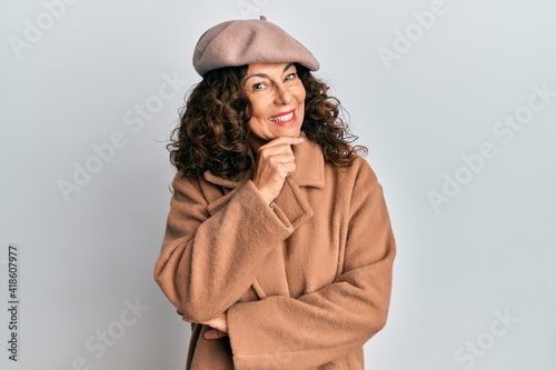 Middle age hispanic woman wearing french look with beret looking confident at the camera with smile with crossed arms and hand raised on chin. thinking positive.