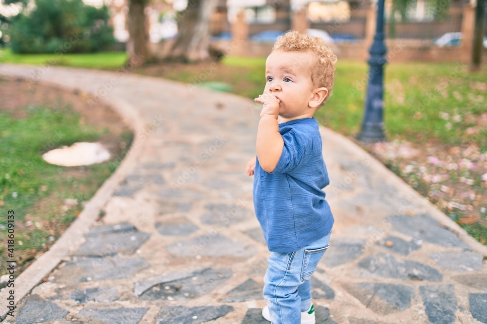 Sad little boy putting fingers on mouth touching gums because toothache at the park on a sunny day. Beautiful blonde hair male toddler in pain for new baby teeth outdoors Sad little boy putting fingers on mouth touching gums because toothache at the park on a sunny day. Beautiful blonde hair male toddler in pain for new baby teeth outdoors
