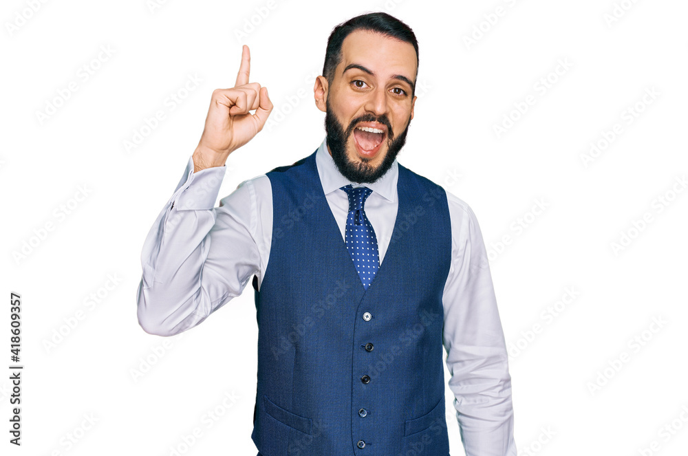 Young man with beard wearing business vest pointing finger up with successful idea. exited and happy. number one. Young man with beard wearing business vest pointing finger up with successful idea. exited and happy. number one.