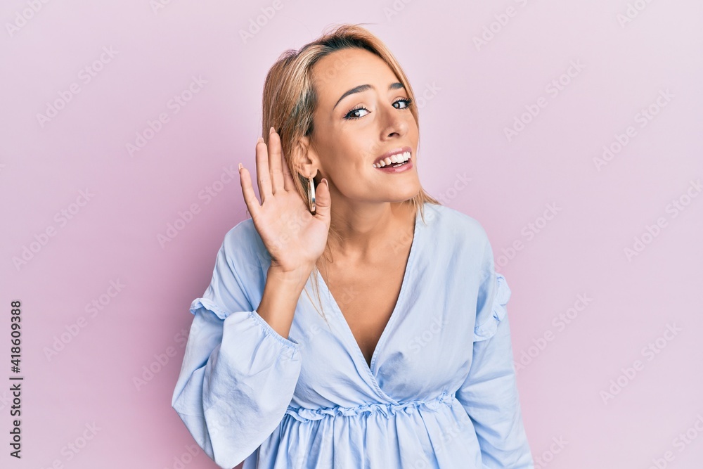 Beautiful blonde woman wearing summer dress smiling with hand over ear listening and hearing to rumor or gossip. deafness concept. Beautiful blonde woman wearing summer dress smiling with hand over ear listening and hearing to rumor or gossip. deafness concept.