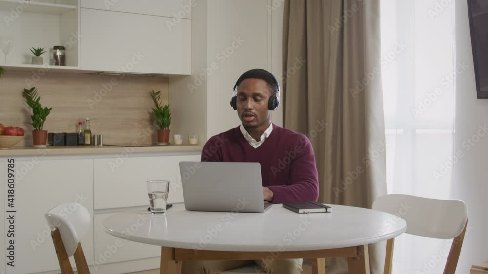 Wide shot of a young african american man in headphones working on a laptop. Close up of a call center emloyee working distant Wide shot of a young african american man in headphones working on a laptop. Close up of a call center emloyee working distant