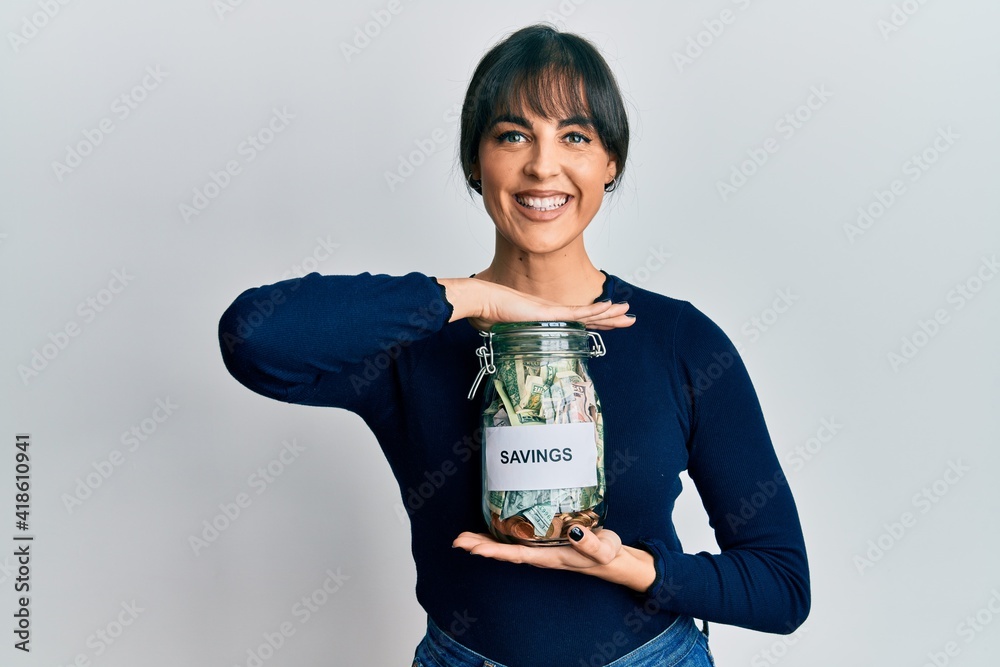 Young hispanic woman holding savings jar smiling with a happy and cool smile on face. showing teeth.