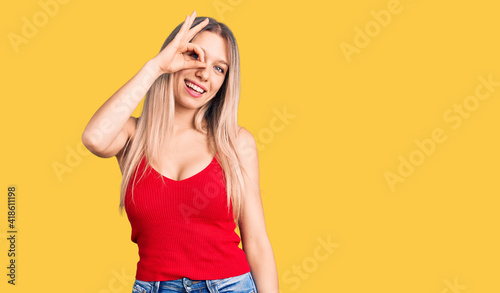 Young beautiful blonde woman wearing casual clothes smiling happy doing ok sign with hand on eye looking through fingers