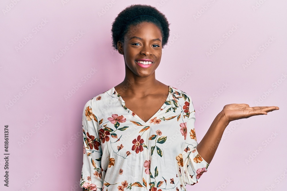 Young african american girl wearing casual clothes smiling cheerful presenting and pointing with palm of hand looking at the camera. Young african american girl wearing casual clothes smiling cheerful presenting and pointing with palm of hand looking at the camera.
