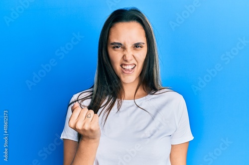 Young hispanic woman wearing casual white t shirt angry and mad raising fist frustrated and furious while shouting with anger. rage and aggressive concept.
