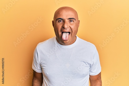 Mature middle east man wearing casual white tshirt sticking tongue out happy with funny expression. emotion concept.