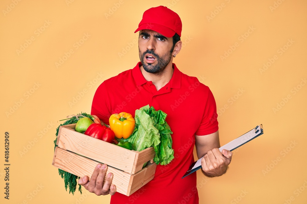 Handsome hispanic man with beard wearing uniform holding delivery food in shock face, looking skeptical and sarcastic, surprised with open mouth Handsome hispanic man with beard wearing uniform holding delivery food in shock face, looking skeptical and sarcastic, surprised with open mouth