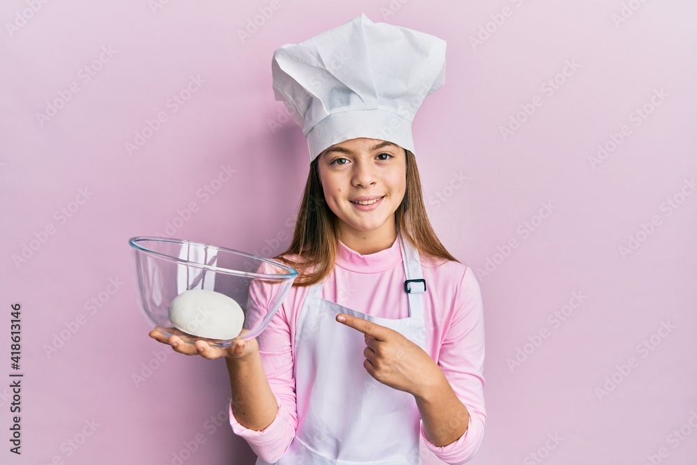 Beautiful brunette little girl wearing chef hat holding bread dough smiling happy pointing with hand and finger Beautiful brunette little girl wearing chef hat holding bread dough smiling happy pointing with hand and finger