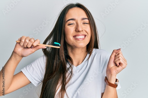 Young hispanic girl holding toothbrush with toothpaste screaming proud, celebrating victory and success very excited with raised arm photo