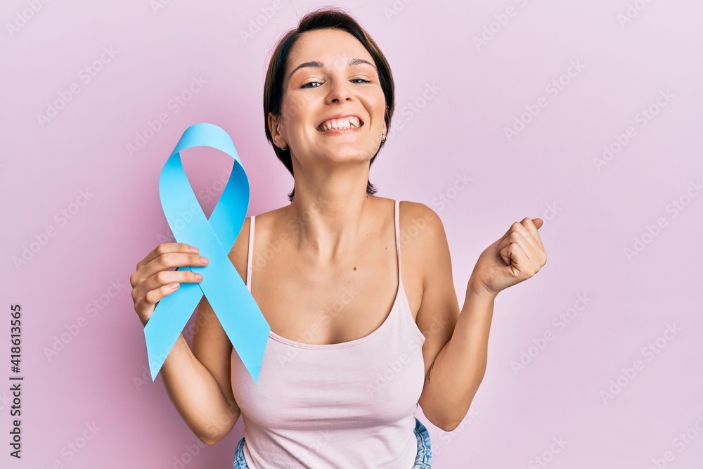 Young brunette woman with short hair holding blue ribbon screaming proud, celebrating victory and success very excited with raised arm Young brunette woman with short hair holding blue ribbon screaming proud, celebrating victory and success very excited with raised arm