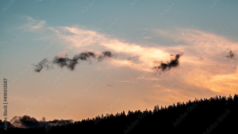 Colorful clouds at sunset pass over a hill covered with trees. Colorful clouds at sunset pass over a hill covered with trees.