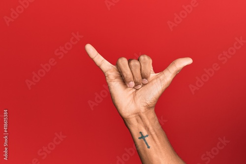 Hand of hispanic man over red isolated background gesturing hawaiian shaka greeting gesture, telephone and communication symbol