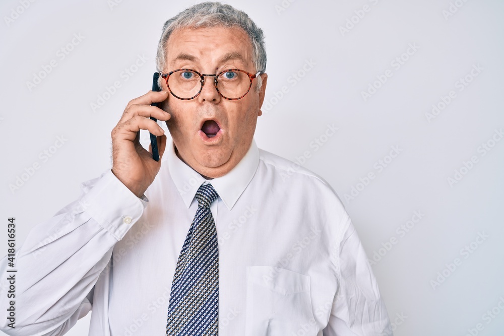 Senior grey-haired man wearing business clothes having conversation talking on the smartphone scared and amazed with open mouth for surprise, disbelief face Senior grey-haired man wearing business clothes having conversation talking on the smartphone scared and amazed with open mouth for surprise, disbelief face