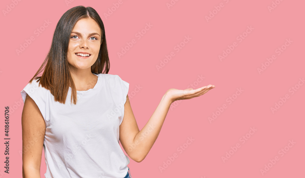 Young caucasian woman wearing casual white tshirt smiling cheerful presenting and pointing with palm of hand looking at the camera. Young caucasian woman wearing casual white tshirt smiling cheerful presenting and pointing with palm of hand looking at the camera.