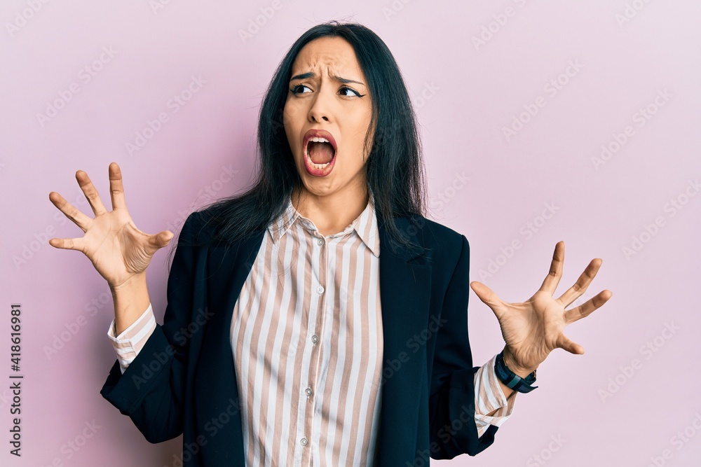 Young hispanic girl wearing business clothes crazy and mad shouting and yelling with aggressive expression and arms raised. frustration concept. Young hispanic girl wearing business clothes crazy and mad shouting and yelling with aggressive expression and arms raised. frustration concept.
