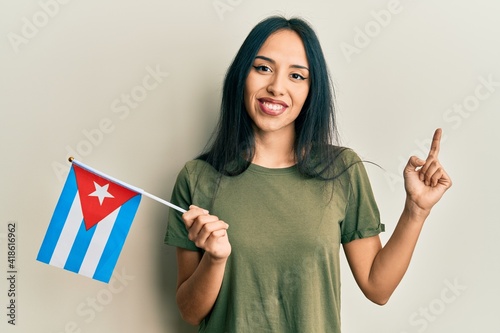 Young hispanic girl holding cuba flag smiling happy pointing with hand and finger to the side