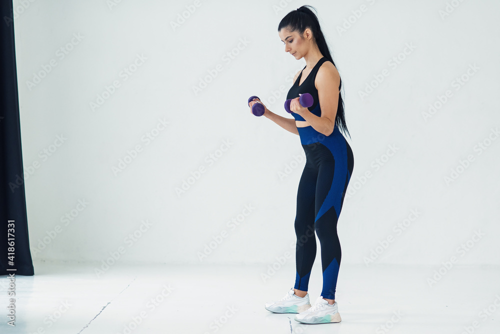 Young beautiful woman doing exercises with dumbbells in fitness studio. Athletic girl enjoying her training process. Young beautiful woman doing exercises with dumbbells in fitness studio. Athletic girl enjoying her training process.