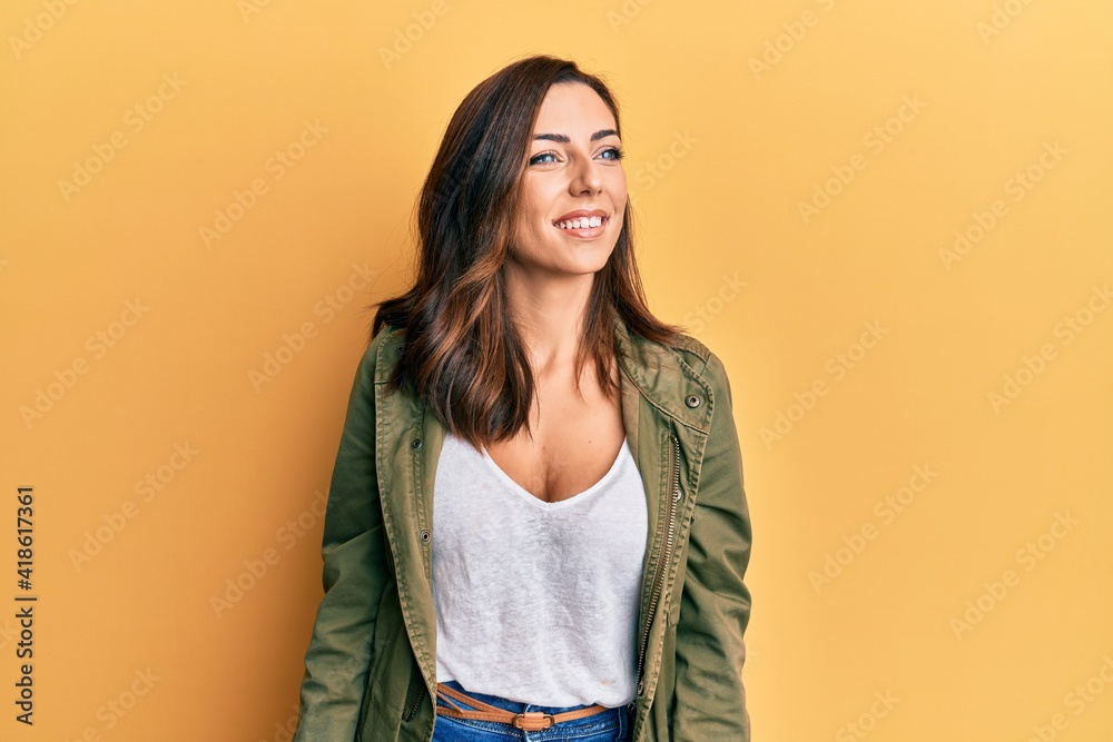 Young brunette woman wearing casual clothes over yellow background looking away to side with smile on face, natural expression. laughing confident. Young brunette woman wearing casual clothes over yellow background looking away to side with smile on face, natural expression. laughing confident.