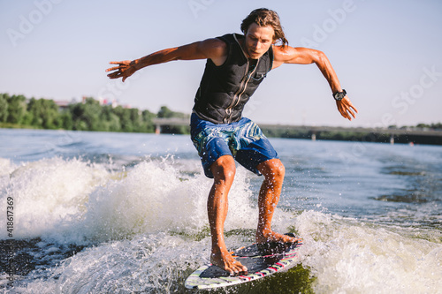 Active wakesurfer jumping on wake board down the river waves. Surfer on wave. Male athlete training on wakesurf training. Active water sports in open air on board. A man catches a wave on surf © Elizaveta