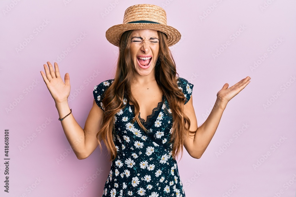 Young brunette woman wearing summer hat celebrating mad and crazy for success with arms raised and closed eyes screaming excited. winner concept Young brunette woman wearing summer hat celebrating mad and crazy for success with arms raised and closed eyes screaming excited. winner concept