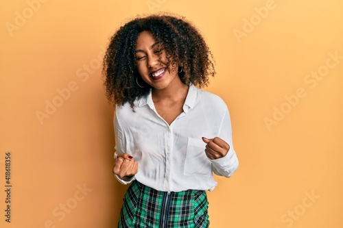 Beautiful african american woman with afro hair wearing scholar skirt very happy and excited doing winner gesture with arms raised, smiling and screaming for success. celebration concept.