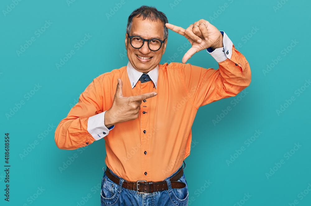 Middle age indian man wearing casual clothes and glasses smiling making frame with hands and fingers with happy face. creativity and photography concept. Middle age indian man wearing casual clothes and glasses smiling making frame with hands and fingers with happy face. creativity and photography concept.