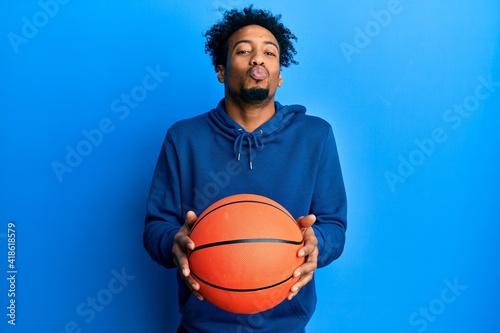 Young african american man with beard holding basketball ball looking at the camera blowing a kiss being lovely and sexy. love expression.