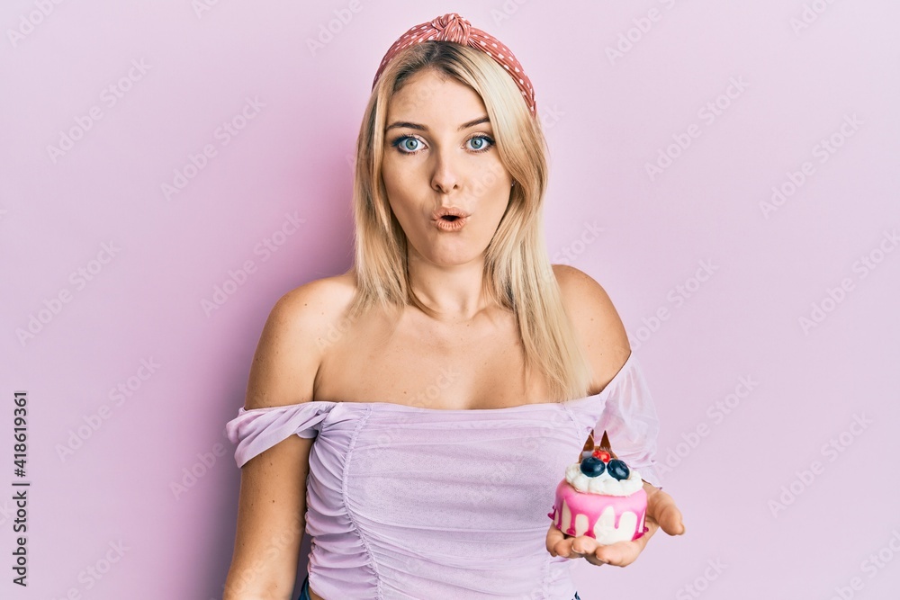 Young caucasian woman holding cake sweets scared and amazed with open mouth for surprise, disbelief face