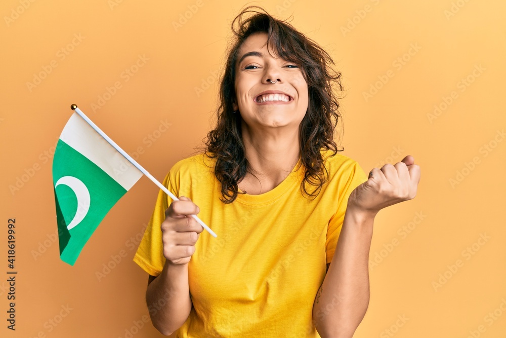 Young hispanic woman holding pakistan flag screaming proud, celebrating victory and success very excited with raised arm Young hispanic woman holding pakistan flag screaming proud, celebrating victory and success very excited with raised arm