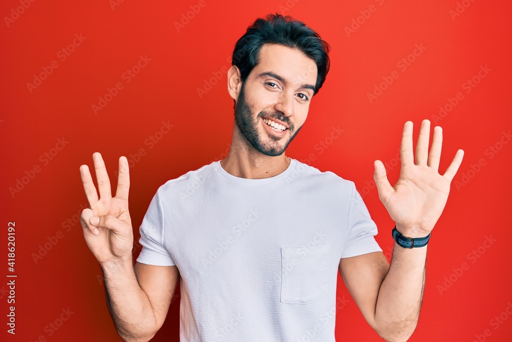 Naklejka premium Young hispanic man wearing casual white tshirt showing and pointing up with fingers number eight while smiling confident and happy.