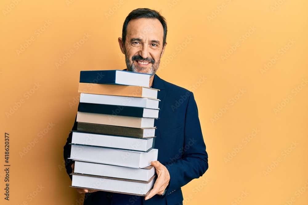 Middle age hispanic man holding a pile of books looking positive and happy standing and smiling with a confident smile showing teeth Middle age hispanic man holding a pile of books looking positive and happy standing and smiling with a confident smile showing teeth