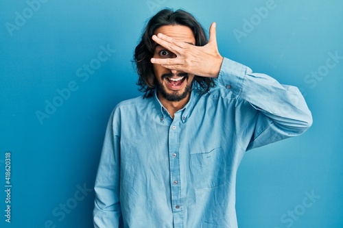Young hispanic man wearing casual clothes peeking in shock covering face and eyes with hand, looking through fingers with embarrassed expression. © Krakenimages.com