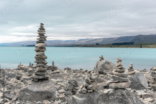 Tall, narrow, rock cairn on the shore of Lake Tekapo, Mackenzie District, New Zealand. The lake and mountains in the background.