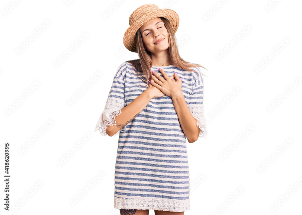 Beautiful caucasian woman wearing summer hat smiling with hands on chest with closed eyes and grateful gesture on face. health concept. Beautiful caucasian woman wearing summer hat smiling with hands on chest with closed eyes and grateful gesture on face. health concept.