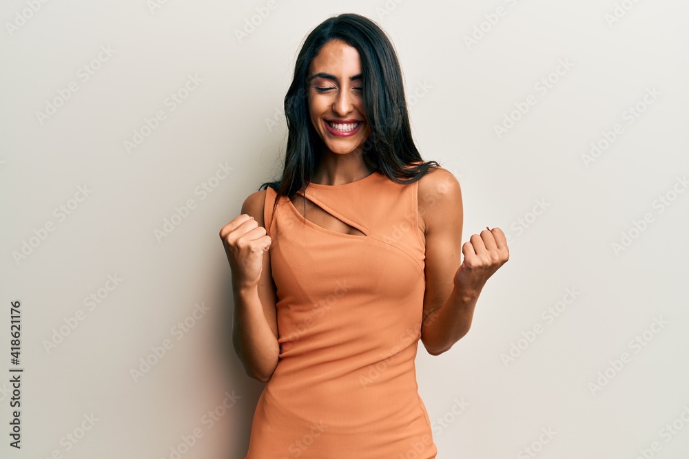 Obraz premium Beautiful hispanic woman wearing summer dress very happy and excited doing winner gesture with arms raised, smiling and screaming for success. celebration concept.