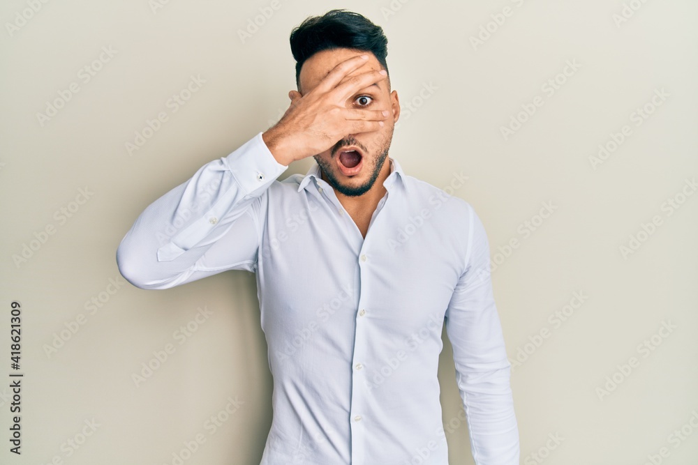 Young arab man wearing casual clothes peeking in shock covering face and eyes with hand, looking through fingers afraid Young arab man wearing casual clothes peeking in shock covering face and eyes with hand, looking through fingers afraid