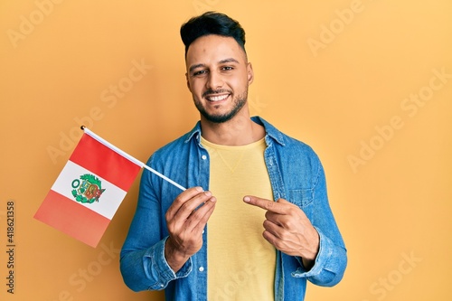 Foto Young arab man holding peru flag smiling happy pointing with hand and finger