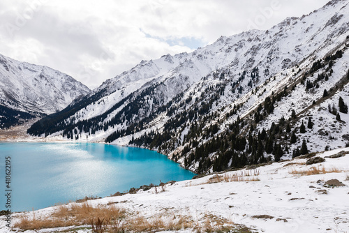 Big Almaty Lake in Kazakhstan in a cold winter day. Plenty of snow visible around the Alpine Lake located in the Trans Ili Alatau mountains.