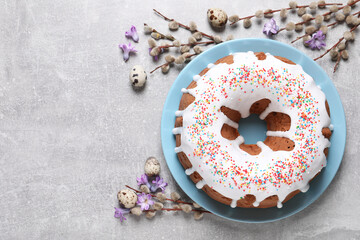 Glazed Easter cake with sprinkles, quail eggs, flowers and willow branches on light table, flat lay. Space for text