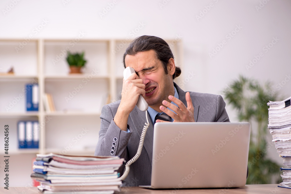 Young male employee unhappy with excessive work in the office Young male employee unhappy with excessive work in the office