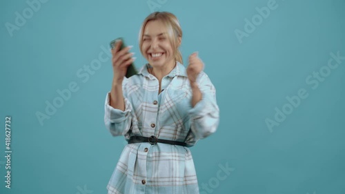The young winner who uses the phone, at the end celebrates the victory by shaking hands Beautiful mature young woman, blonde, in a shirt, blue. Isolated on blue background, Concept of life. People's