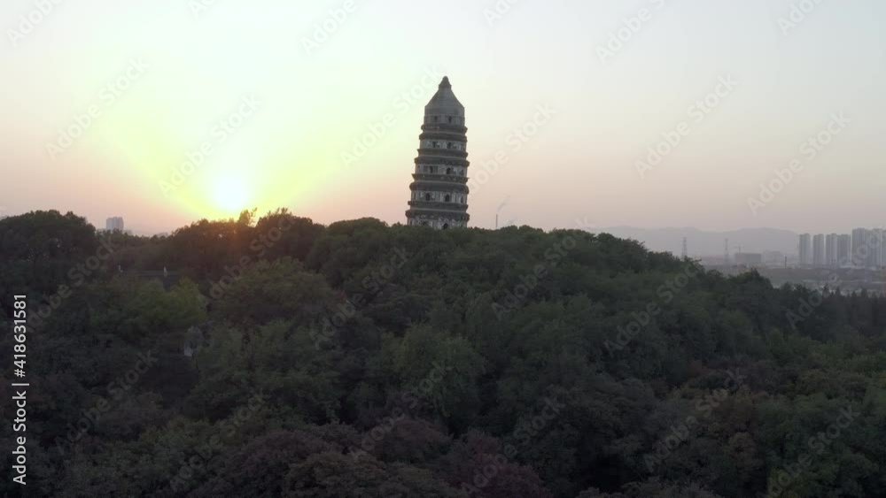 Aerial panning shot of Tiger Hill Pagoda amidst trees against sky, drone ascending over famous landmark in city at sunset - Suzhou, China Aerial panning shot of Tiger Hill Pagoda amidst trees against sky, drone ascending over famous landmark in city at sunset - Suzhou, China