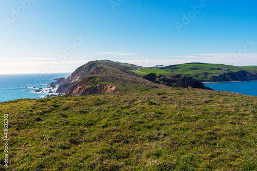 View of Pacific Ocean coastline, with winter green grass covering cliffs and bluffs of Point Reyes Headlands on a sunny day at Point Reyes National Seashore, California.