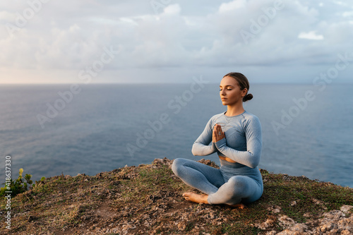 Beautiful woman doing yoga on a cliff, behind an amazing view in the ocean Bali Indonesia