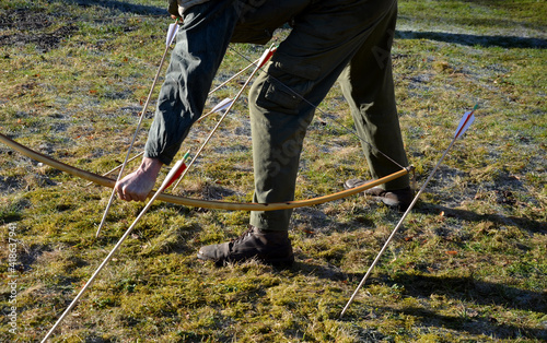 the archer draws a bow and arrow to a shot from a traditional yew bow used in the medieval battles of Agincourt. meadow and wooden curved bow from one piece photo