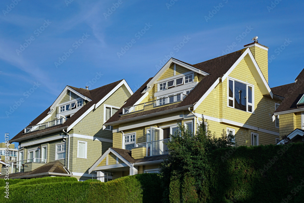 Row of pastel colored clapboard houses with upper level balconies and evergreen hedges Row of pastel colored clapboard houses with upper level balconies and evergreen hedges
