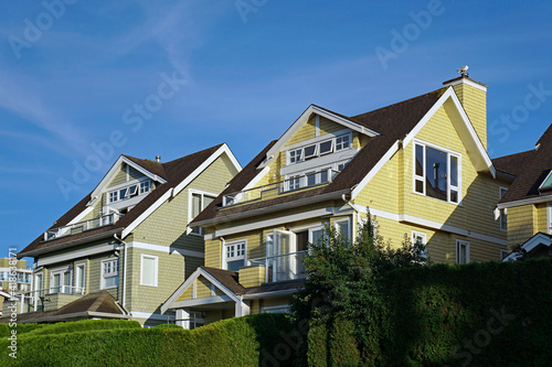 Row of pastel colored clapboard houses with upper level balconies and evergreen hedges © Spiroview Inc.
