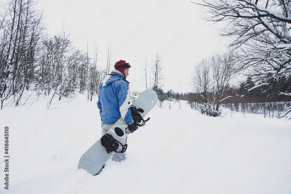 The guy snowboarding goes on a snowy slope. He is holding a snowboard