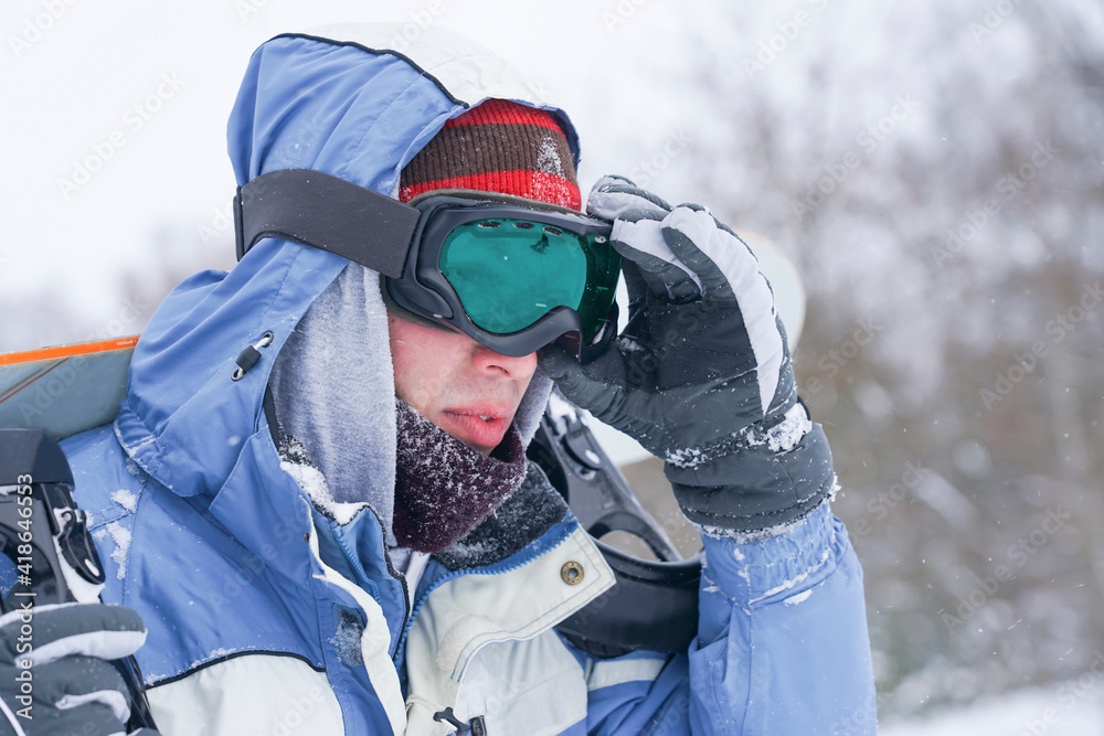 Portrait of a snowboarder on a snowy slope. Freerider with a snowboard in a hat and a mountain mask