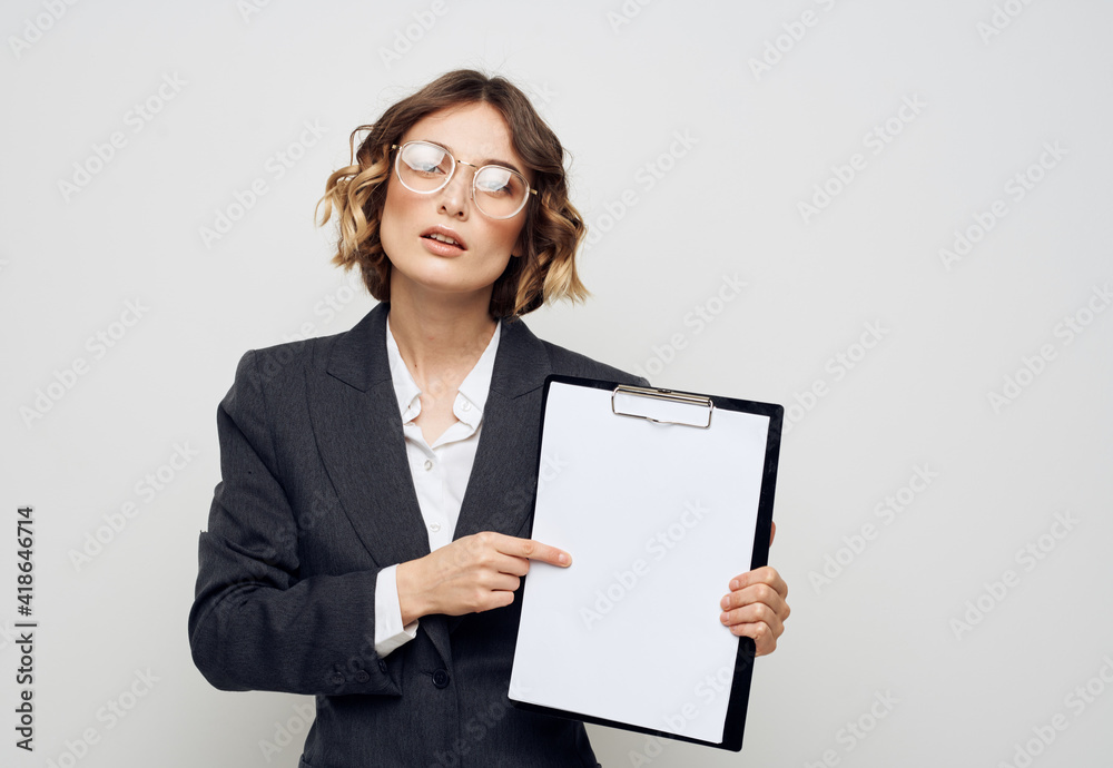 Business woman with documents gestures with her hands on a light background and glasses on her face Business woman with documents gestures with her hands on a light background and glasses on her face